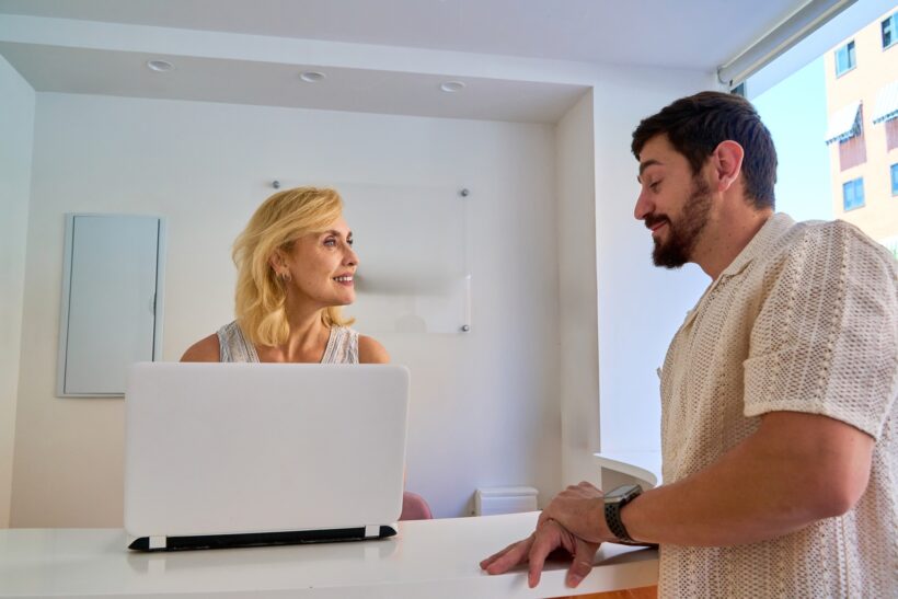 Woman and man having a conversation at a reception desk with a laptop